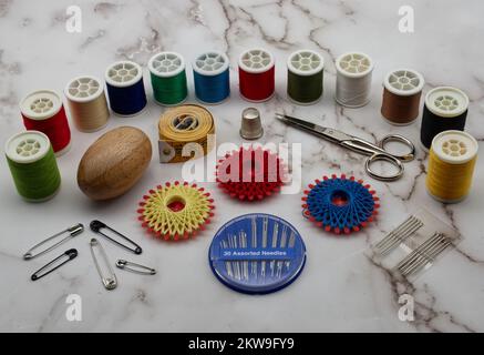 Sewing tools and accessories: scissors, tape measure, spools of thread, needle, thimble and pins isolated on marble background. Stock Photo