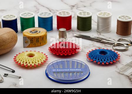 Sewing tools and accessories: scissors, tape measure, spools of thread, needle, thimble and pins isolated on marble background. Stock Photo