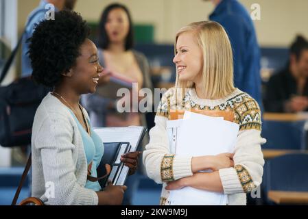 Class is in session. two university students talking together in a lecture hall. Stock Photo