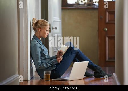 Jotting down a few ideas. A young woman sitting on the floor doing some researching on her laptop. Stock Photo