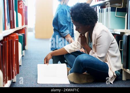 Cramming some last minute knowledge. A young woman sitting on the floor and reading in a library. Stock Photo