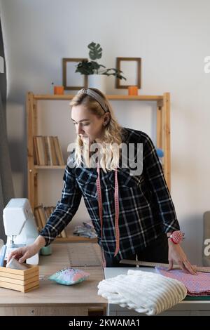 Seamstress at work. Dressmaker making clothes in modern studio. Female Tailor marking fabric on table. Copy space Stock Photo