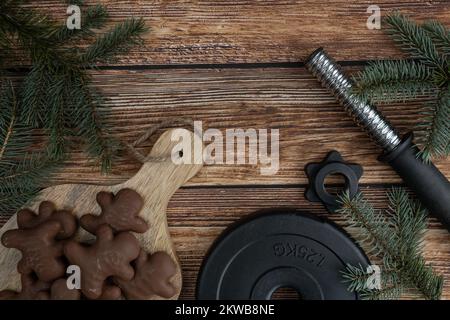 Chocolate gingerbread Christmas cookies, tree branches, dumbbell weight plate. Fitness holiday season winter diet composition. Gym workout concept. Stock Photo