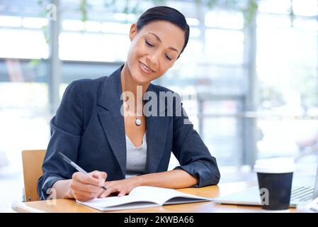 Taking minutes for the meeting. A businesswoman writing on a notebook while sitting in her office. Stock Photo