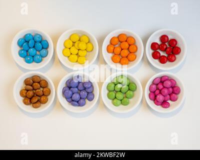 eight bowls of individually colored candy on a white background Stock Photo