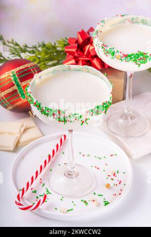 White sugar cookie martini with festive sprinkles rim. Christmas New Year alcohol cocktail with colorful red green sugar sprinkles, on Christmas decor Stock Photo