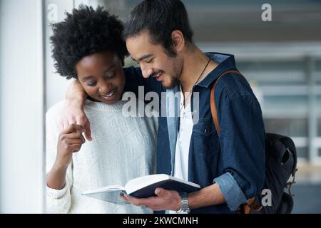 Going over their last minute revision before they hit their exam. a student couple standing in the University halls looking at a text book together. Stock Photo