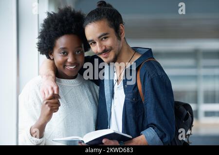 Their life long love started at College. Portrait of a college couple holding hands with a text book in front of them. Stock Photo