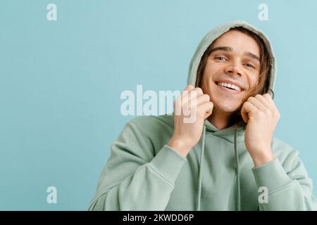 Young handsome man with long hair holding hood and looking in camera over isolated blue background Stock Photo