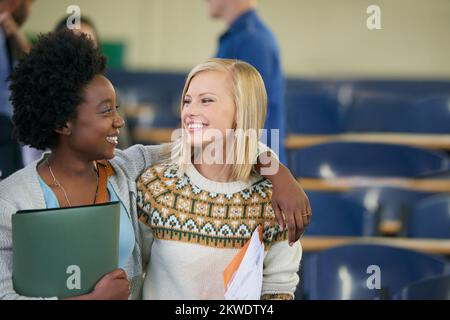 We aced that exam. two university students talking together in a lecture hall. Stock Photo