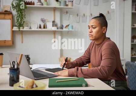 Side view portrait of black young woman using pen tablet while working on new designs in studio, copy space Stock Photo
