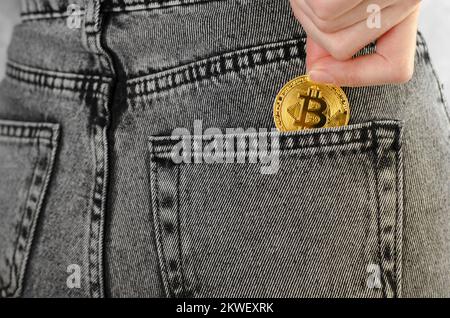 Bitcoin in a woman's hand close-up. A woman's hand puts a Bitcoin in the back pocket of her jeans. Cryptocurrency Stock Photo