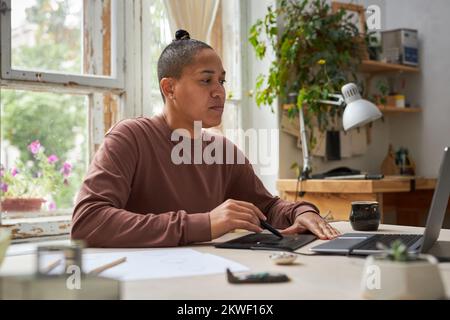 Side view portrait of female artist using graphic tablet with laptop in creative studio Stock Photo