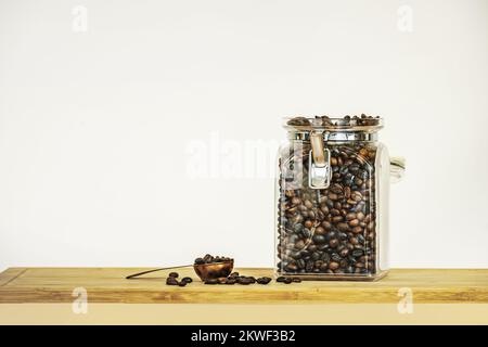 A glass jar filled with roasted coffee with a full copper spoon on a bamboo board Stock Photo