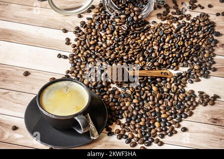 A cup of fresh coffee on a wooden table full of overturned coffee beans from a can Stock Photo