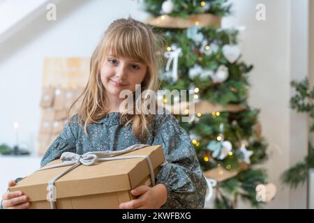 Little girl with a gift near the Christmas tree at home Stock Photo