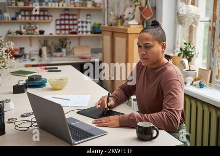 Creative black woman working on new designs in studio and using pen tablet Stock Photo