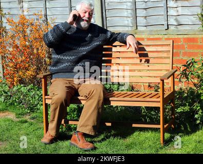 elderly or senior man sitting outside and using his mobile phone. Stock Photo