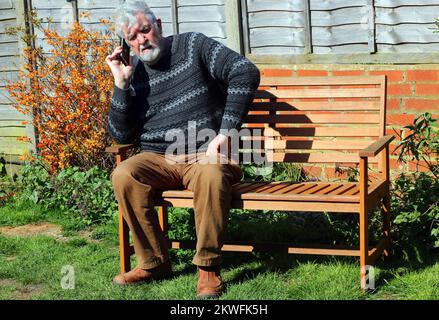 elderly or senior man sitting outside and using his mobile phone. Stock Photo