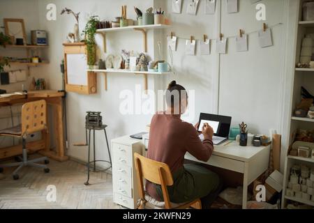 Back view of female artist working with laptop in cozy studio interior, copy space Stock Photo