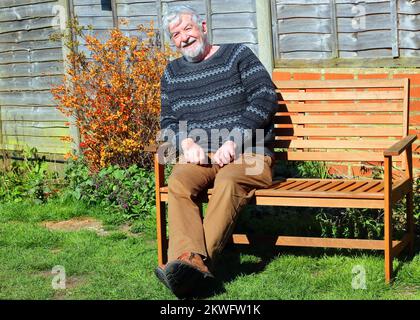 Senior or elderly man sitting outside on a bench and smiling towards the camera. Stock Photo