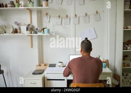 Back view of artist using laptop in minimal workshop studio, copy space Stock Photo