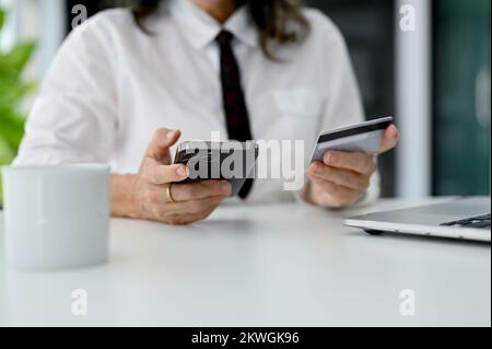 cropped image, An aged woman holding a credit card and using her smartphone to pay an online bills. Stock Photo