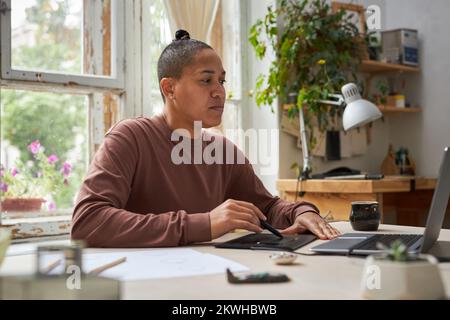 Side view portrait of female artist using graphic tablet with laptop in creative studio Stock Photo