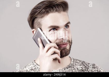 Man thoughtful dreamy use smartphone communication, grey background. Communication concept. Guy attractive well groomed with beard and hairstyle talk Stock Photo