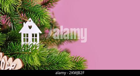 Banner with Christmas tree decorated with white house shaped  tree ornament baubles on pink background with empty copy space Stock Photo
