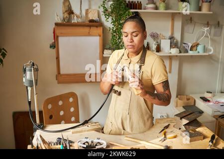 Portrait of black female jeweler working on new creations at wooden table with tools, copy space Stock Photo