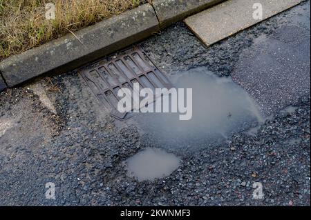 Blocked drain and pothole in poorly maintained road in England. Stock Photo