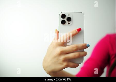 iPhone apple 13 mini in female hands,smartphone phone isolated on white hand with multi-colored manicure Stock Photo
