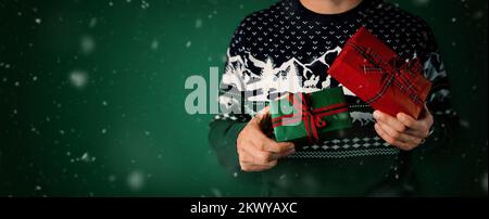 man in christmas sweater holding wrapped gift boxes in hands on green background. banner with copy space Stock Photo