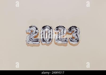 Christmas or New Year background. Beige color flat lay with silver shiny 2023 balloon numbers in the center. Simple minimalistic greeting card. Stock Photo