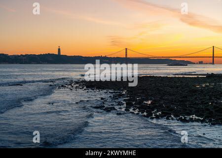 Tagus River (Rio Tejo) at sunset with 25 de Abril Bridge and Sanctuary of Christ the King skyline on background - Lisbon, Portugal Stock Photo