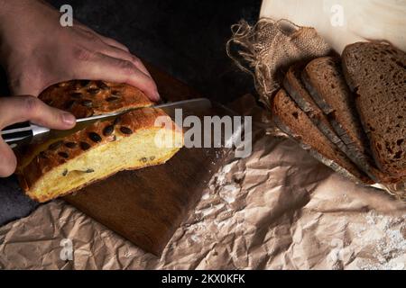 Men's hands are cutting bread on the table. Next to the slices of sliced bread on the background of crumpled wrapping paper. Flat lay . The concept of eco-friendly goods, small business. Stock Photo