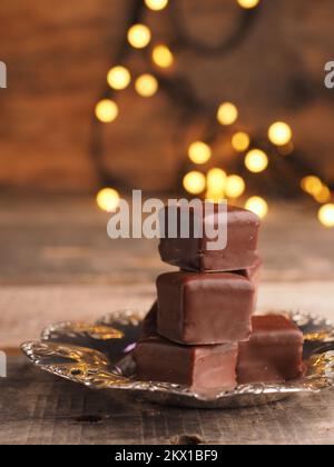 Stacked chocolate dices on a silver plate on a wooden table with Christmas lights Stock Photo