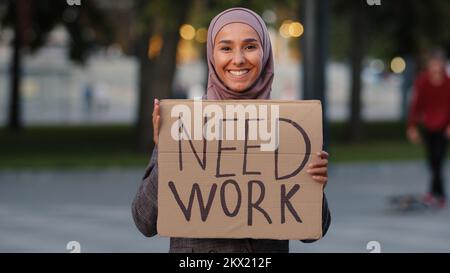 Happy muslim woman in hijab standing outdoors islamic ethnic girl smiling unemployed lady female waving hello greeting pointing with finger on Stock Photo