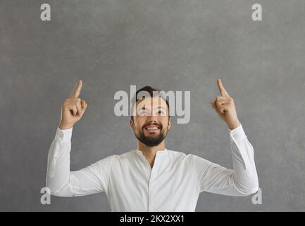 Happy young man smiling and pointing up with both index fingers at copy space above Stock Photo