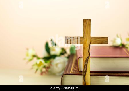 Religion composition with wooden cross with closed red Christian bibles with white flowers on a light gradient background with copy space. Easter holi Stock Photo