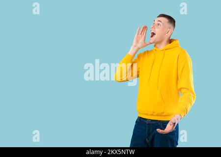 Positive caucasian man yelling towards copy space, holding hand next to mouth, making announcement Stock Photo