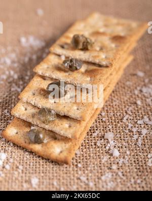 Some wholegrain crackers are stacked like a stairway, with capers and rock salt on and around Stock Photo