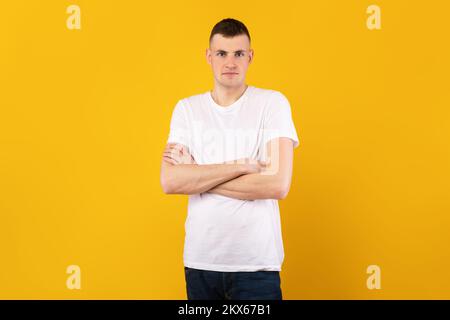 Male portrait. Handsome caucasian guy with folded arms looking at camera, wearing t-shirt, posing over yellow background Stock Photo