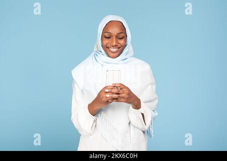 Joyful african american muslim woman holding modern smartphone, looking at gadget screen and smiling Stock Photo