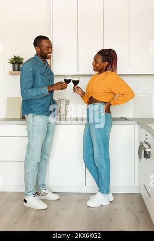Domestic romance. African american couple drinking wine, standing in kitchen interior, full length shot Stock Photo