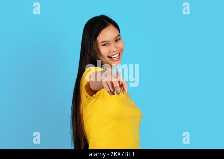 Smiling confident millennial korean lady in yellow t-shirt point finger at camera, isolated on blue background Stock Photo