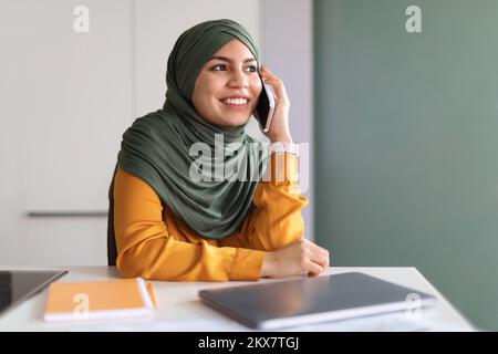 Smiling Muslim Woman In Hijab Talking On Mobile Phone In Office Stock Photo