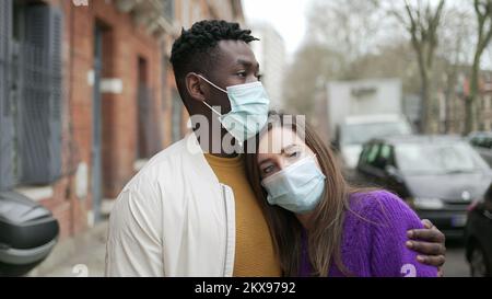 Interracial couple wearing covid-19 face mask standing outside in street Stock Photo