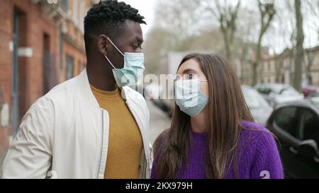 Interracial couple wearing covid-19 face mask standing outside in street Stock Photo